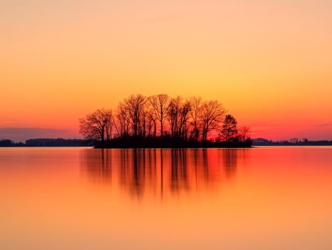 sunset or sunrise reflected in the water with a tree-topped island – inspiration for a weekly list of free educational events and resources for the association community