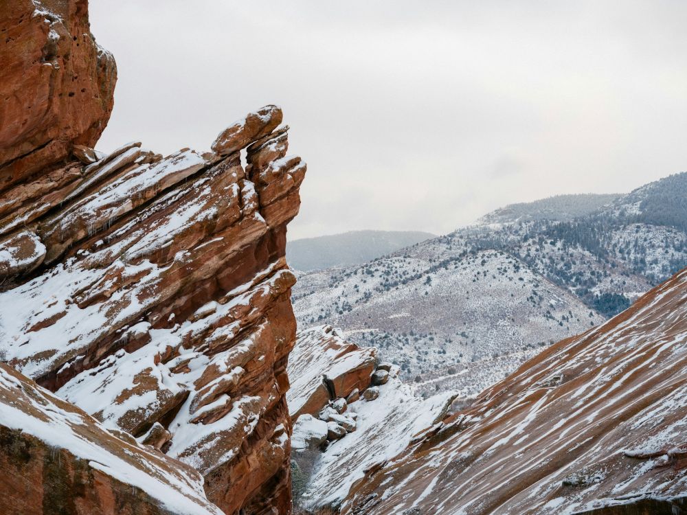 red rock ledge dusted with snow with mountains in the distance