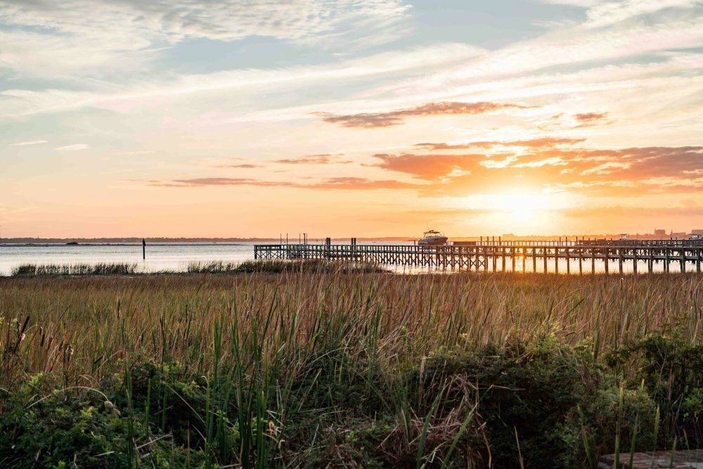 view from marsh grasses of the sun setting over the coastal water and pier in South Carolina